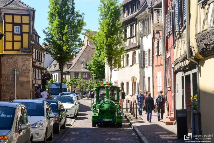 A colorful tourist train vehicle is seen navigating the old cobblestone streets of Colmar in Alsace, France.
