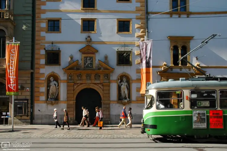 On Herrengasse in the historic city center of Graz, Austria, a tram is passing the ornate facade of the Landhaus building.
