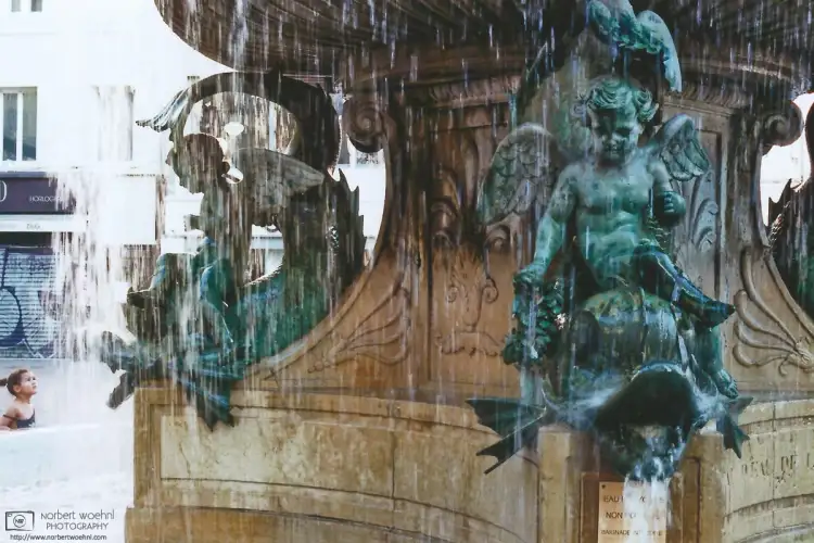 A girl is watching the Old City Fountain on Place Grenette in Grenoble, France.