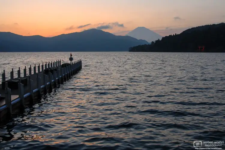 An evening view across Lake Ashi in Hakone, Japan, with Mount Fuji visible in the background.