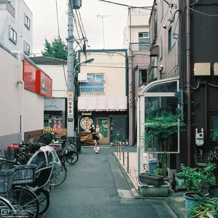 A young mother carrying her child is turning the corner at a side street supermarket in the Jujo area of Kita Ward in Tokyo, Japan.