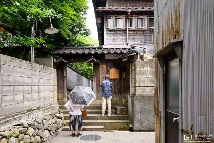 Visitors are seen reading an information board outside the side entrance to Myōryūji Temple in Kanazawa, Japan.