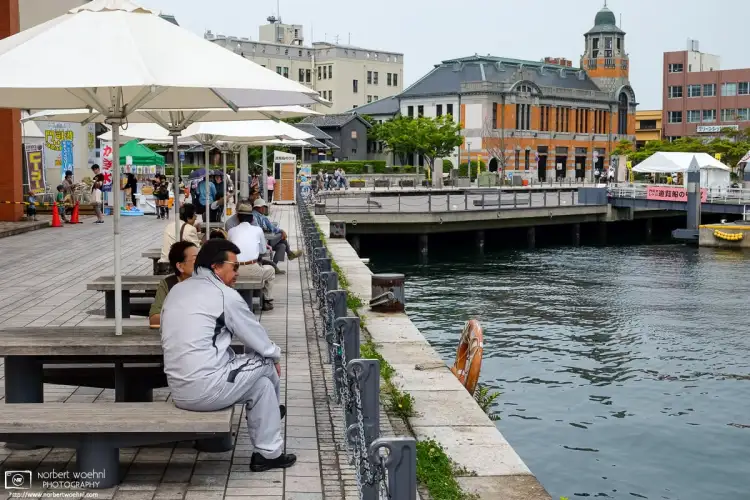 At Mojiko Retro Port in Kitakyushu, Japan, a man vaguely reminiscent of Elvis is looking out on the water. The Old Mitsui Lines Building is visible in the back.