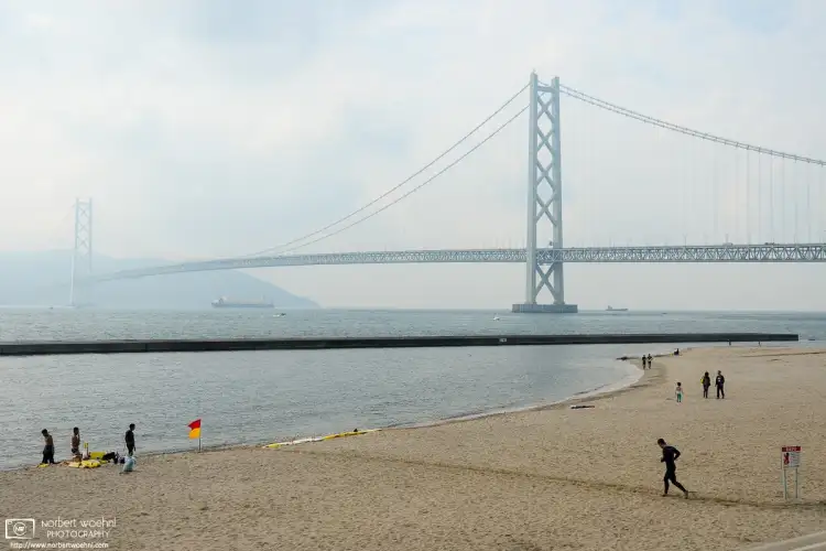 Beachside activities against the backdrop of Akashi Kaikyō, the beautiful suspension bridge in Kobe, Japan.