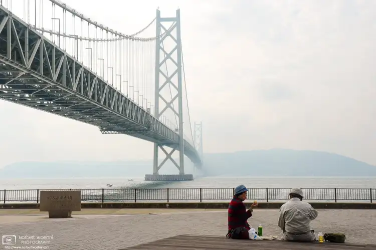 Along the water front on the northern side of Akashi Kaikyō Bridge in Kobe, Japan, folks are pictured having a snack.