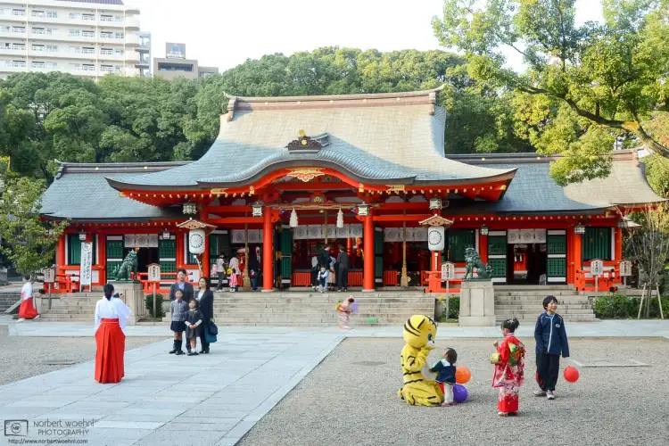 Visitors and shrine maiden are engaging in various activities outside the main hall of Ikuta Shrine in Kobe, Japan.
