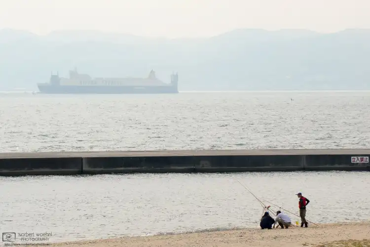 Fishing at Marine Pier in Kobe, Japan, with a container ship passing in the background.