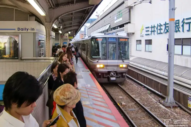 Waiting commuters and platform glances during arrival of a train at Sannomiya Station in Kobe, Japan.
