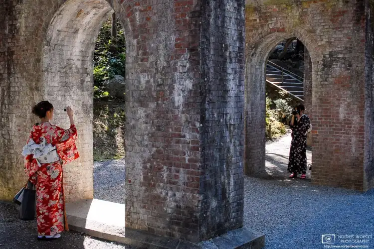 Two young women in kimono photographing each other under the aqueduct at Nanzenji Temple in eastern Kyoto, Japan.
