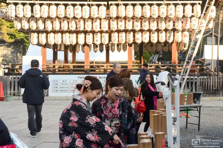 Two women in kimono are reading Omikuji (fortune-telling paper strips) at Yasaka Shrine in the Gion district of Kyoto, Japan.
