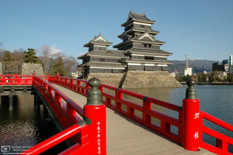 A view of Matsumoto Castle in Nagano Prefecture, Japan, across a red bridge on its western side.