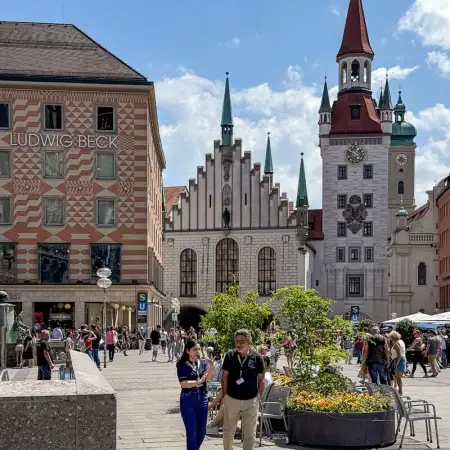 On Marienplatz in the city center of Munich, Germany, two people are having a chat during lunch break. The white building in the back is the Old Town Hall.