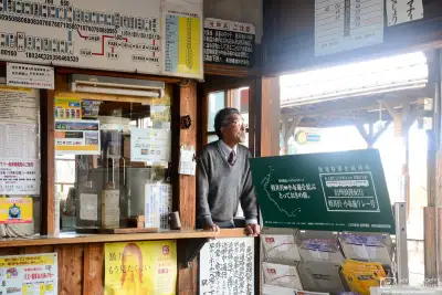 Photo of the Station Master peeking out of his office at Matsushiro Station, a station that has become disused since. It used to be a stop on the Yashiro Line of the Nagano Electric Railway Company.