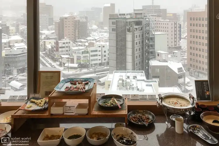 Part of a hotel breakfast buffet in Nagano, Japan, with an outside view of the city scenery on a snowy day.