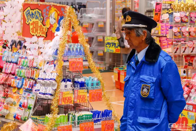 A colorfully dressed guard standing outside a drugstore with even more colorful merchandise. Seen in a shopping street in the Ōsu district of Nagoya, Japan.
