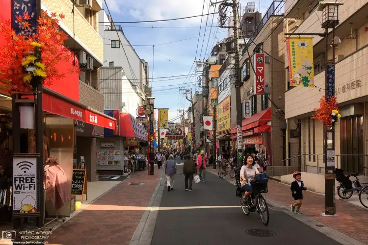 A boy is joyfully running beside his bicycling mother on Sugamo Jizodori Shopping Street in the Toshima Ward of Tokyo, Japan.