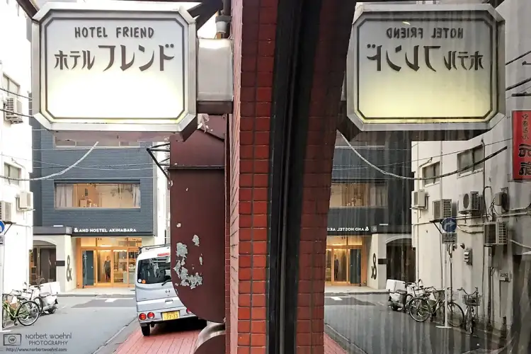 In the Taito Ward of Tokyo, Japan, a Showa-era hotel sign is reflected in a window, opening up a view towards a quiet backstreet with a more contemporary hotel.