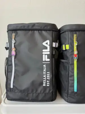 Two key rings with illustrations of a male and a female character in kickboxing sports gear, attached to zippers on two sports bags.