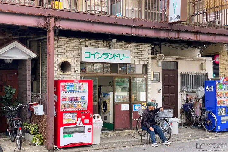 A man sitting on a chair is watching life outside a coin laundry in Kirigaoka in the Kita Ward of Tokyo, Japan.