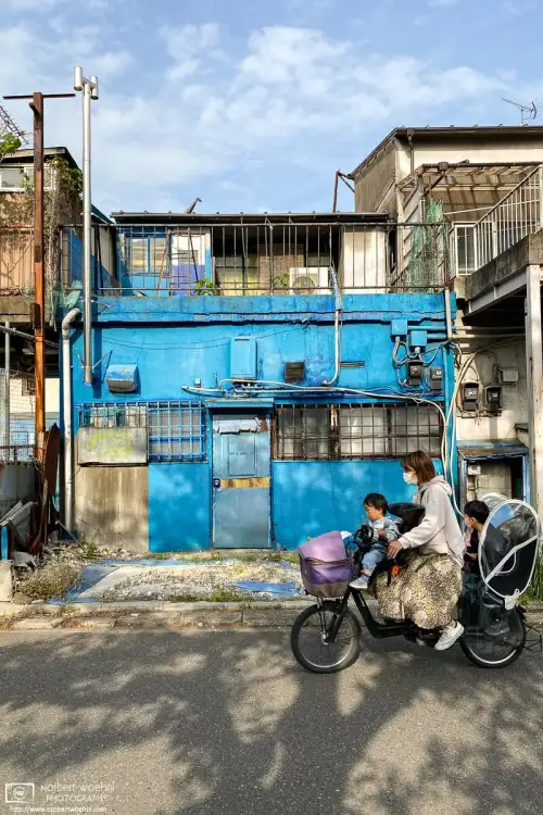 A fully occupied bicycle passes a colorful building in the Kirigaoka area of Kita ward in Tokyo, Japan.