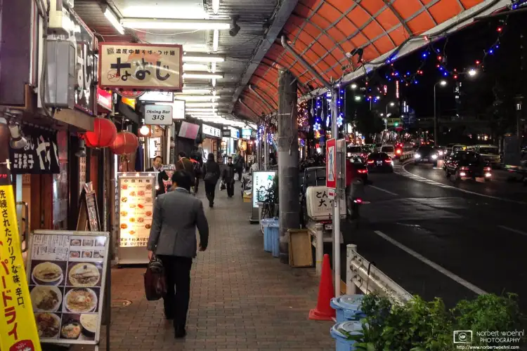 At the end of his working day, a salaryman is seen walking along Meguro Dori in Tokyo, Japan, exploring dinner options.