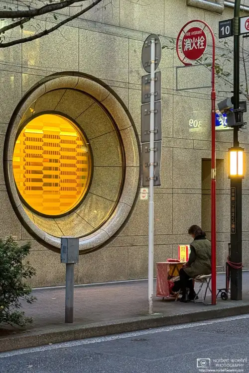 On an early evening outside a department store in the Nihonbashi area of Tokyo, Japan, a fortune teller is seated on the sidewalk and waiting for clients.