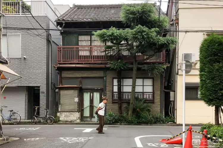 An old woman is looking at the photographer while walking through a neighborhood in Taito-ku, Tokyo, Japan.